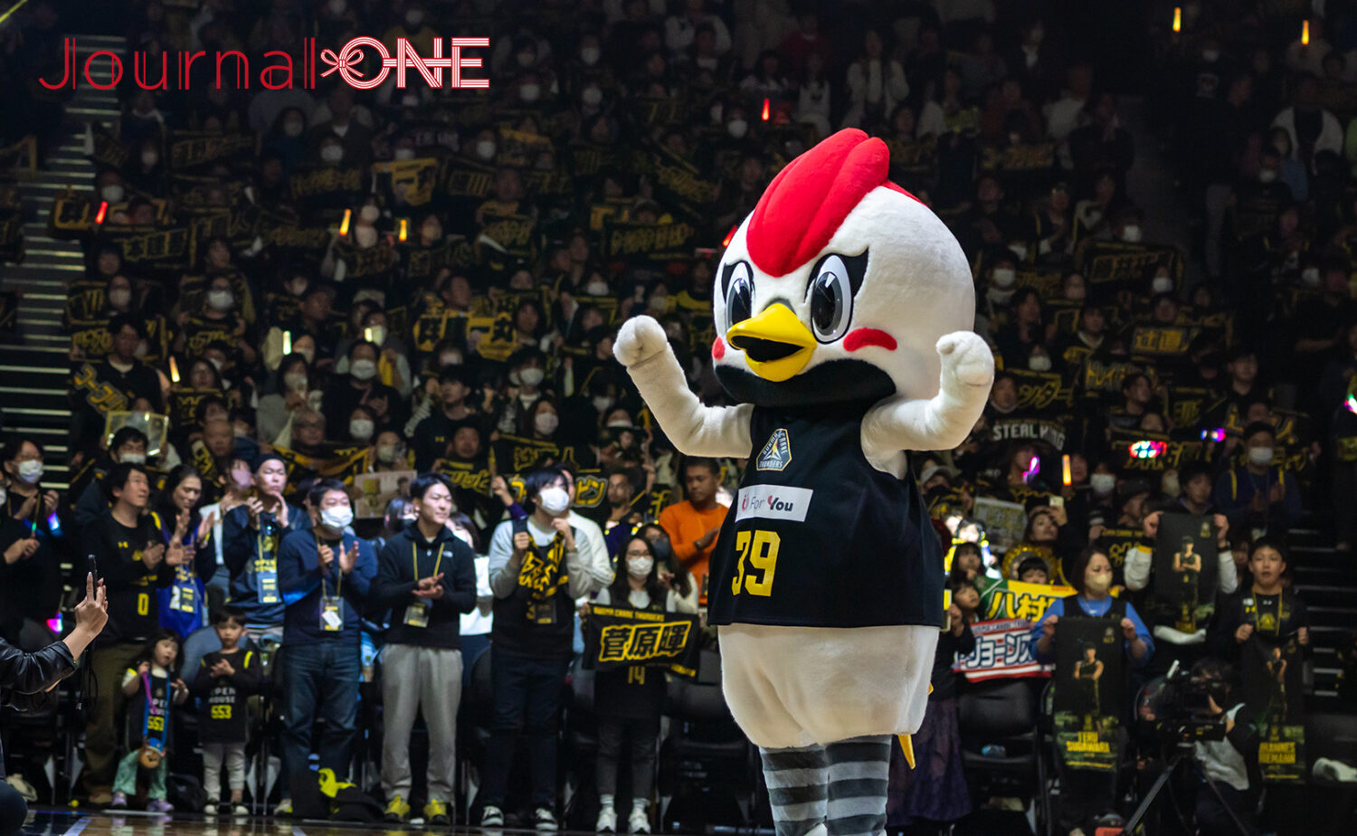 群馬クレインサンダーズ公式マスコット「サンダくん」が、満員の観客で埋め尽くされたオープンハウスアリーナ太田のコート上で、元気にポーズを決めている様子。