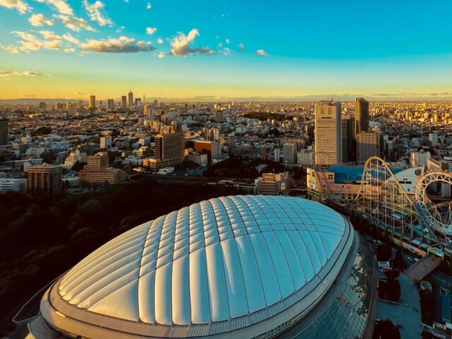 夕暮れに輝く東京ドームと都心の街並み。ライスボウル開催地として知られる東京ドームの外観と、背後に広がるビル群と遊園地のジェットコースターが見える風景
