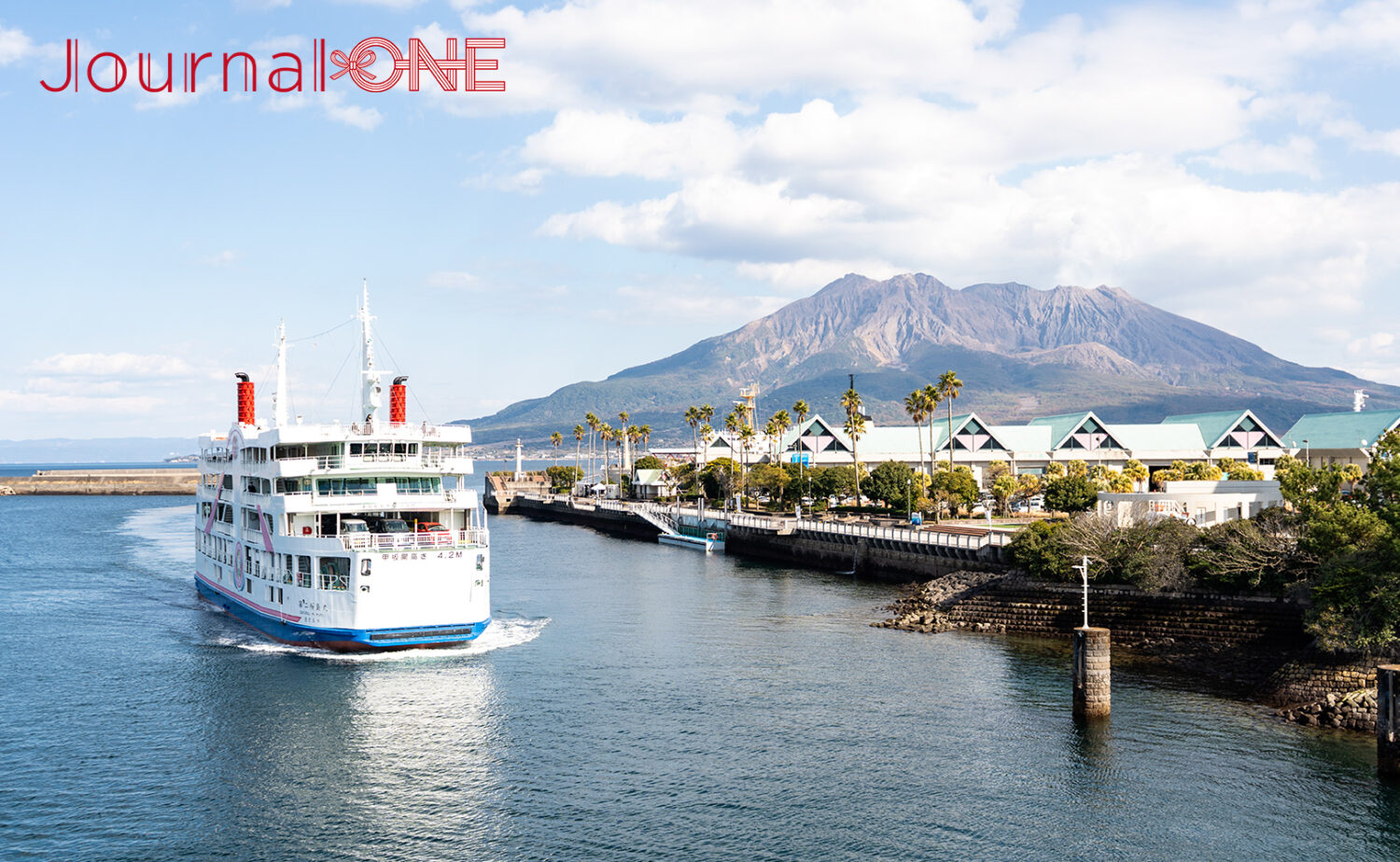 雄大な桜島を背景に鹿児島港を出港する「第二桜島丸」。白地にピンクとブルーのラインが入った船体は桜島 観光 モデルコースで外せない桜島フェリーが、青い海と空に映える美しい風景。