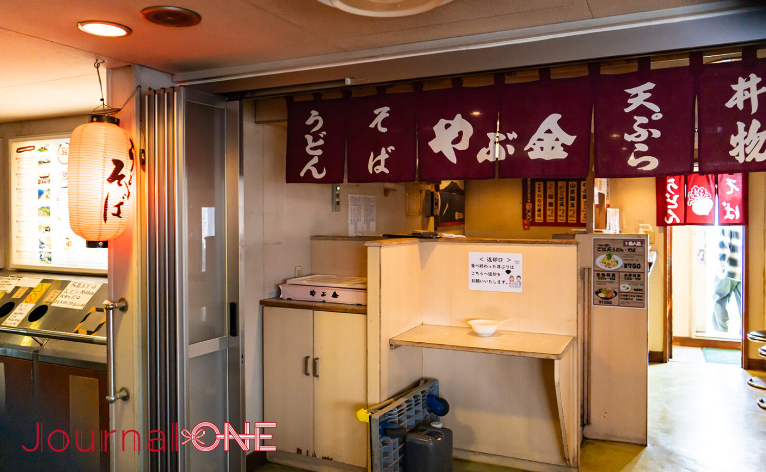 船内にある名物うどん店「やぶ金」。赤紫色ののれんに「うどん・そば」の文字が並び、提灯が灯る。わずか15分の船旅の間に多くの乗客が立ち寄る、フェリーの象徴的な風景。