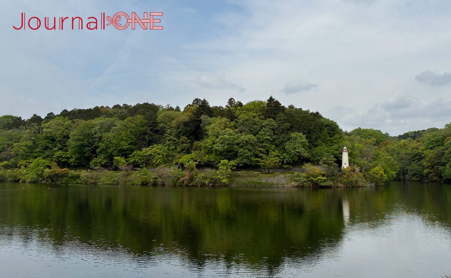 埼玉県飯能市の宮沢湖。対岸にはムーミンバレーパークの豊かな森が広がり、水辺に佇む白い灯台が水面に映り込む。初夏の柔らかな光に照らされた新緑と静かな湖面のパノラマ風景。