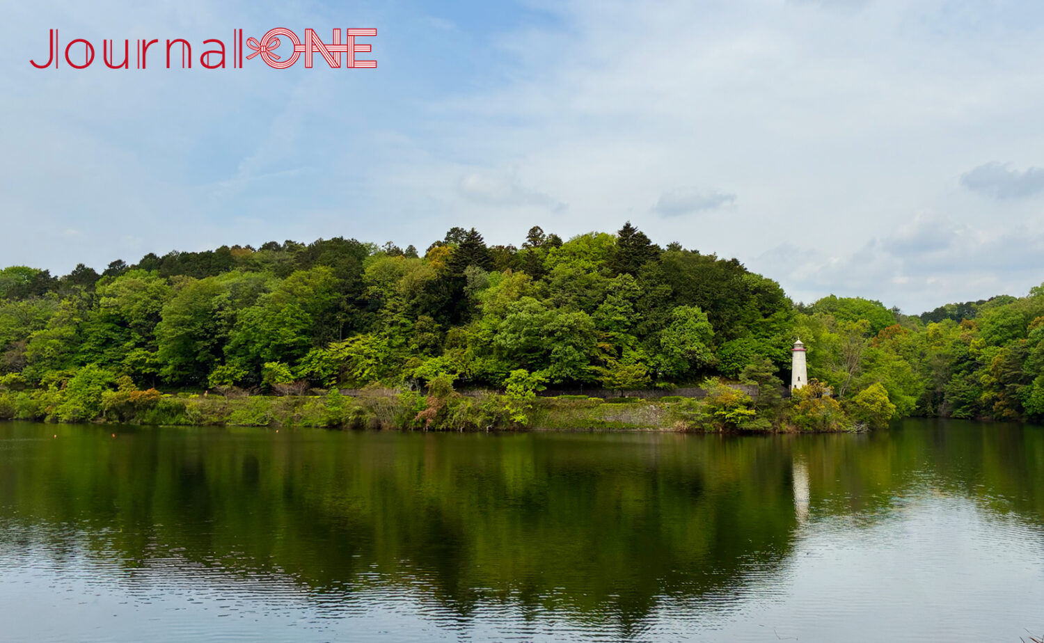 埼玉県飯能市の宮沢湖。対岸にはムーミンバレーパークの豊かな森が広がり、水辺に佇む白い灯台が水面に映り込む。初夏の柔らかな光に照らされた新緑と静かな湖面のパノラマ風景。