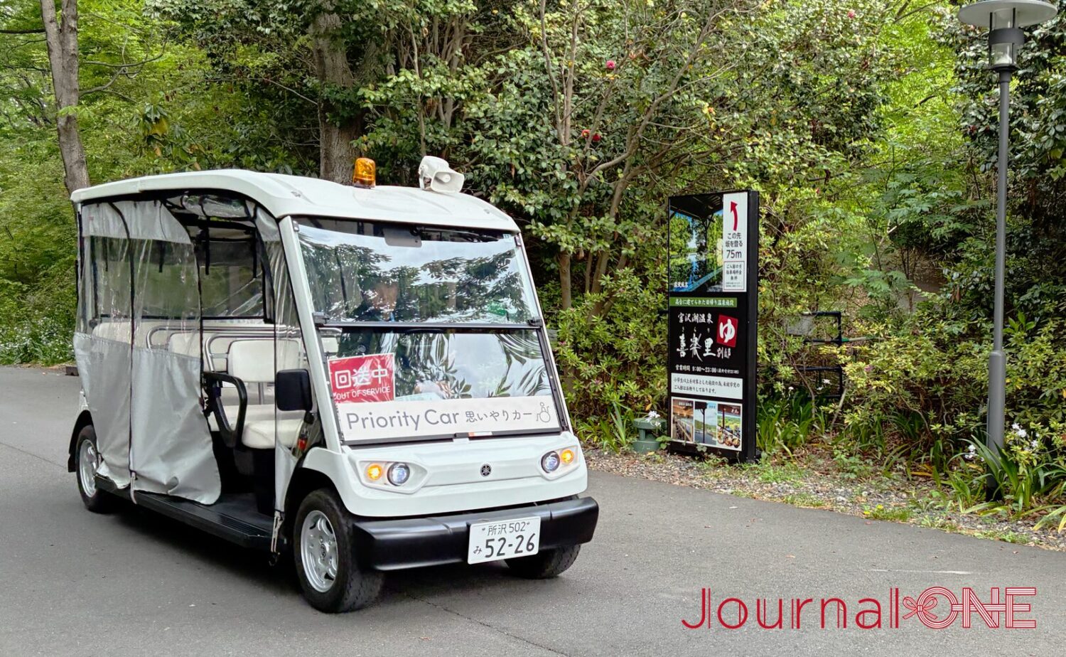 ムーミンバレーパーク内を走行する「おもいやりカー（Priority Car）」。豊かな緑を背景に、白い電動のオープン車両が路面を走る様子。
